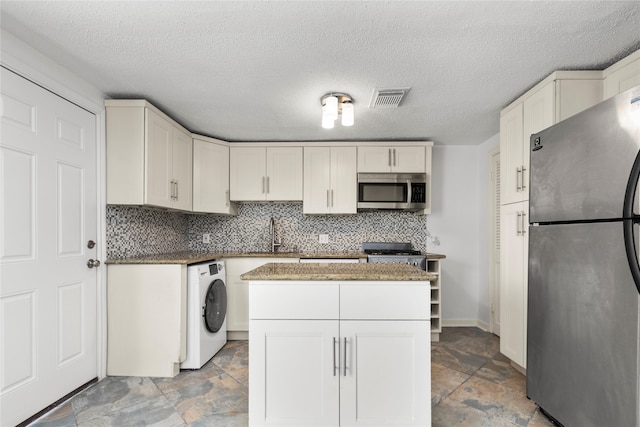 kitchen with washer / clothes dryer, a textured ceiling, appliances with stainless steel finishes, and white cabinets