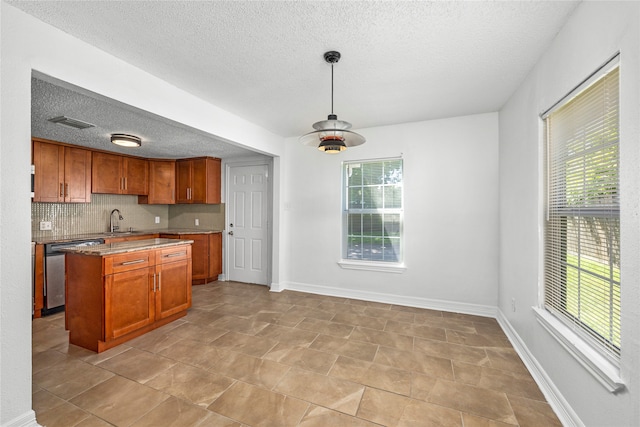 kitchen with decorative backsplash, a kitchen island, pendant lighting, a textured ceiling, and stainless steel dishwasher