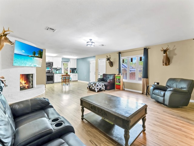 living room with a brick fireplace and light hardwood / wood-style floors