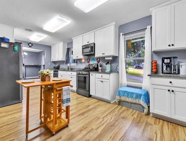 kitchen featuring a textured ceiling, appliances with stainless steel finishes, light wood-type flooring, and white cabinetry