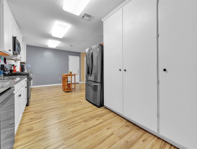 kitchen featuring a textured ceiling, light hardwood / wood-style flooring, white cabinetry, appliances with stainless steel finishes, and light stone countertops