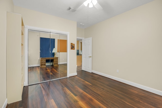 unfurnished bedroom featuring dark wood-type flooring, a closet, a fireplace, and ceiling fan