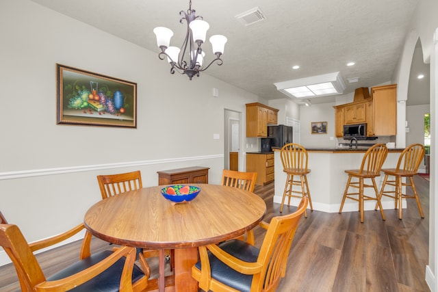 dining room with wood-type flooring, an inviting chandelier, sink, and a textured ceiling