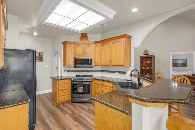 kitchen with sink, kitchen peninsula, decorative backsplash, light hardwood / wood-style flooring, and appliances with stainless steel finishes