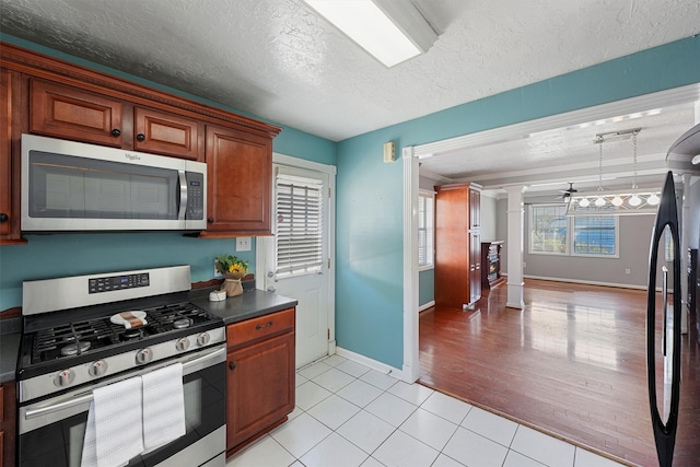 kitchen featuring ornamental molding, a textured ceiling, stainless steel appliances, light wood-type flooring, and ornate columns