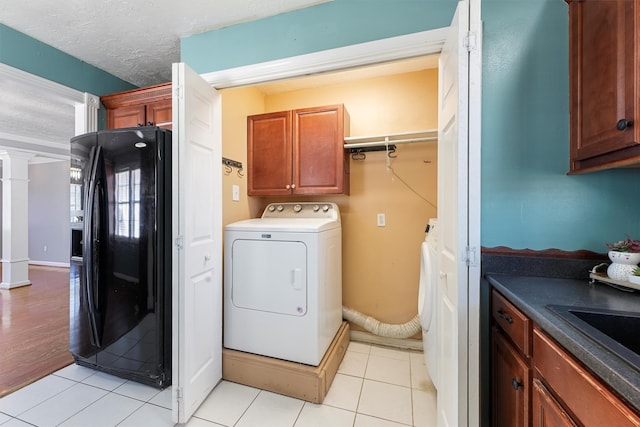 laundry area with light tile patterned floors, a textured ceiling, washer / clothes dryer, cabinets, and ornate columns