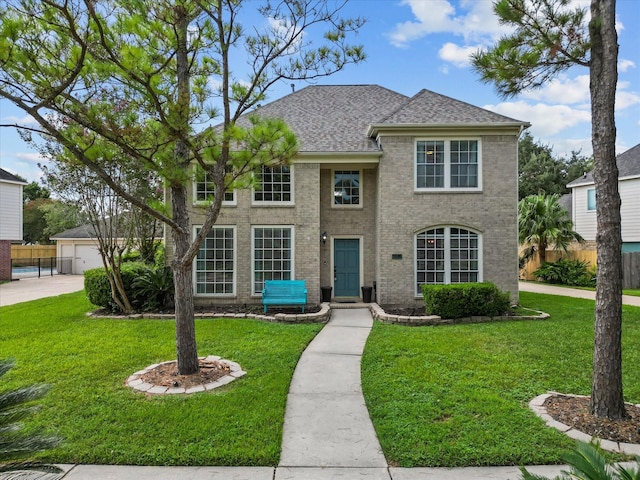 view of front of home with a shingled roof, fence, a front lawn, and brick siding