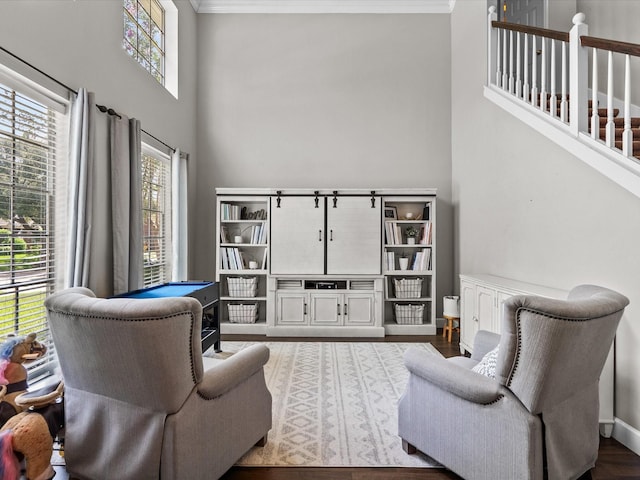 living room featuring a towering ceiling, ornamental molding, a wealth of natural light, and wood finished floors