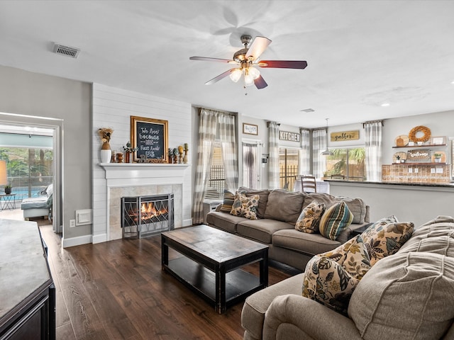 living area featuring a fireplace, wood finished floors, visible vents, baseboards, and a ceiling fan