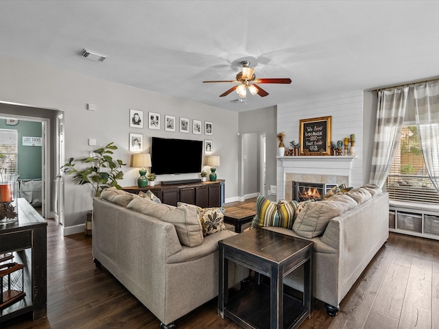 living area with ceiling fan, a fireplace, visible vents, and dark wood finished floors