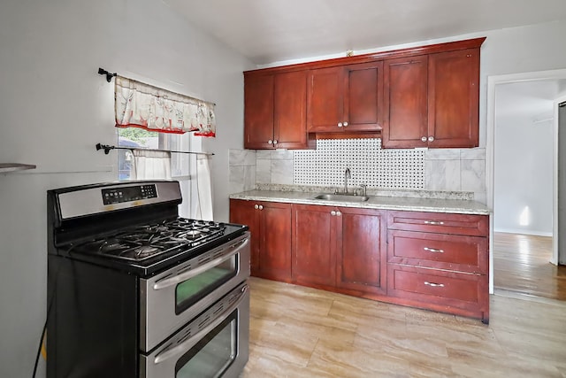 kitchen featuring stainless steel range with gas cooktop, light hardwood / wood-style floors, sink, and tasteful backsplash