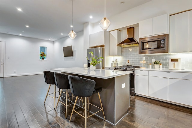 kitchen featuring wall chimney exhaust hood, stainless steel appliances, white cabinetry, and a center island