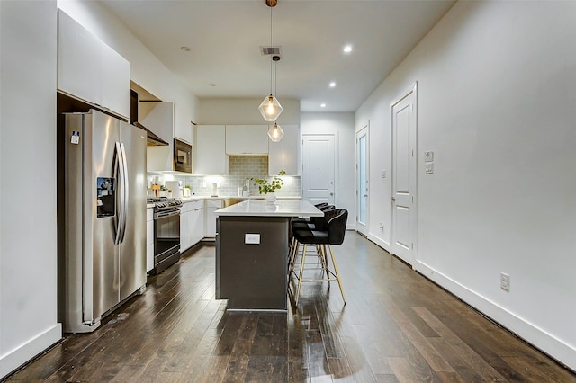 kitchen with appliances with stainless steel finishes, white cabinetry, a kitchen island, decorative light fixtures, and dark hardwood / wood-style floors