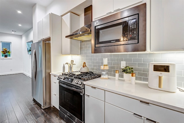 kitchen featuring dark hardwood / wood-style floors, white cabinetry, wall chimney exhaust hood, backsplash, and appliances with stainless steel finishes