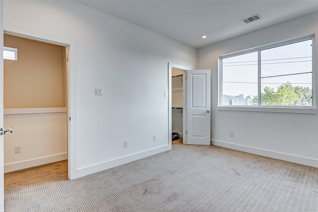 unfurnished bedroom with light carpet and a walk in closet