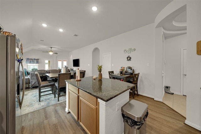 kitchen featuring dark stone countertops, light wood-type flooring, a center island, ceiling fan, and stainless steel fridge with ice dispenser