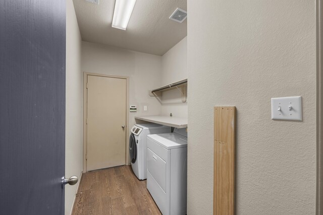 washroom with hardwood / wood-style flooring, washing machine and dryer, and a textured ceiling