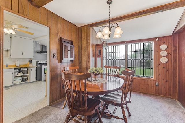 carpeted dining room featuring wooden walls, ceiling fan with notable chandelier, and beam ceiling