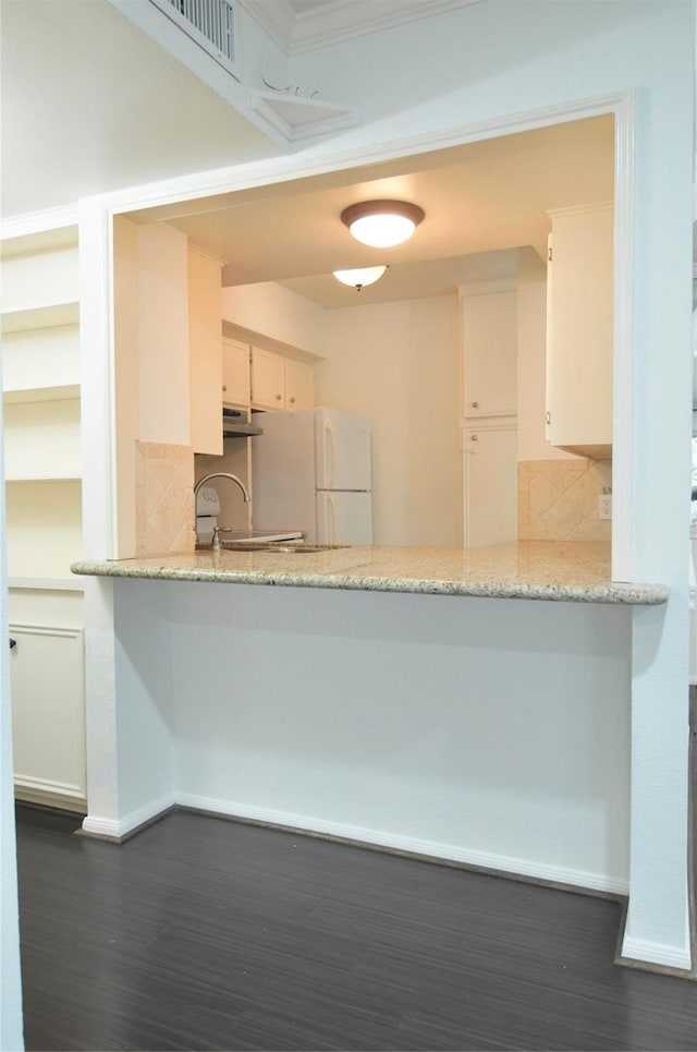 kitchen featuring light stone counters, white refrigerator, backsplash, white cabinetry, and dark hardwood / wood-style flooring