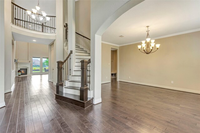 foyer entrance with a towering ceiling, an inviting chandelier, crown molding, and dark wood-type flooring