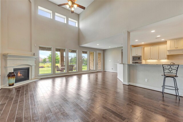 unfurnished living room featuring ceiling fan, dark hardwood / wood-style floors, a towering ceiling, and a healthy amount of sunlight