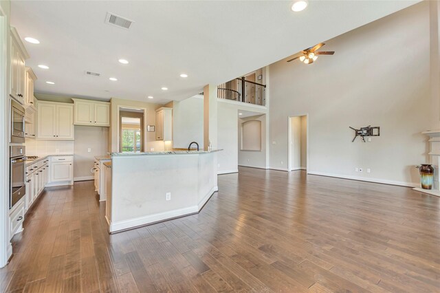 kitchen with light stone counters, ceiling fan, appliances with stainless steel finishes, and dark wood-type flooring