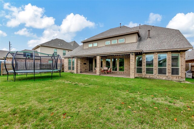 rear view of property with a lawn, a trampoline, and a patio area