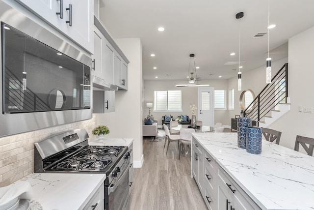 kitchen featuring appliances with stainless steel finishes, hanging light fixtures, light hardwood / wood-style floors, backsplash, and a breakfast bar area