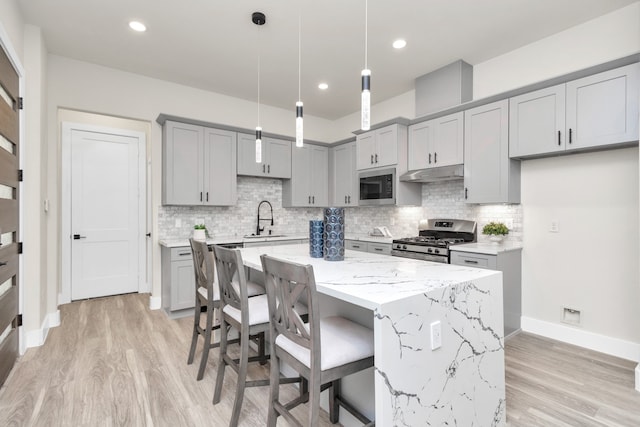 kitchen featuring hanging light fixtures, light hardwood / wood-style floors, a kitchen island, stainless steel appliances, and sink