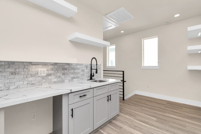 kitchen with light wood-type flooring, backsplash, sink, and light stone counters