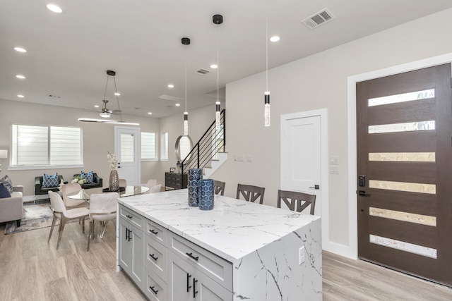 kitchen featuring white cabinetry, a kitchen island, light hardwood / wood-style flooring, decorative light fixtures, and light stone countertops