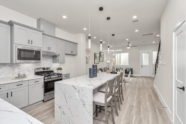 kitchen featuring appliances with stainless steel finishes, a kitchen island, light stone countertops, and ceiling fan