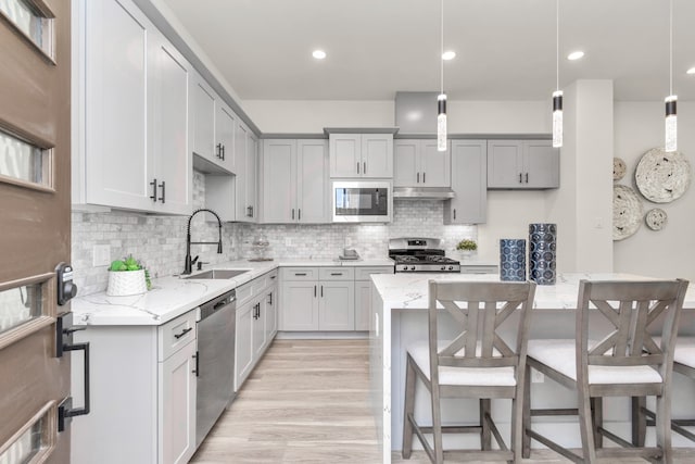 kitchen featuring light stone countertops, stainless steel appliances, decorative light fixtures, and light hardwood / wood-style flooring