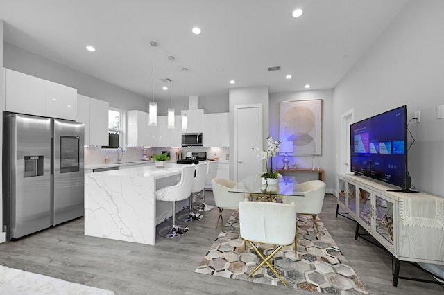 kitchen featuring pendant lighting, white cabinets, a kitchen island, stainless steel appliances, and light wood-type flooring