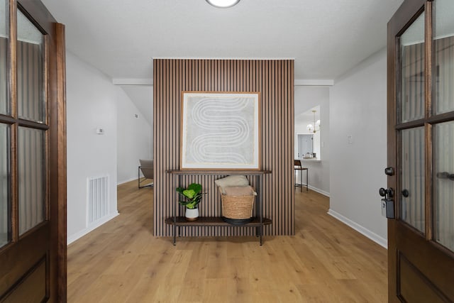 hallway featuring light hardwood / wood-style flooring, a textured ceiling, and an inviting chandelier