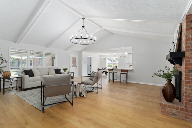 living room with light wood-type flooring, a textured ceiling, a notable chandelier, a fireplace, and vaulted ceiling with beams