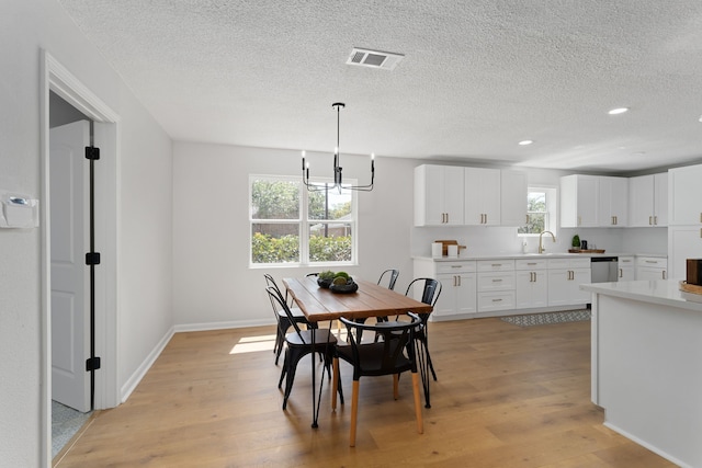 dining space featuring light wood-type flooring, a chandelier, a healthy amount of sunlight, and sink