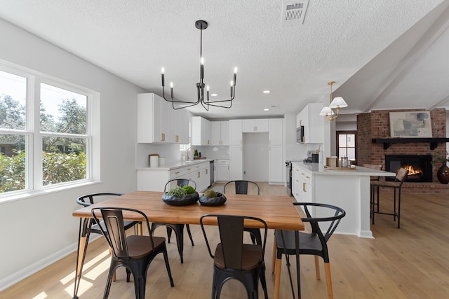 dining room with light hardwood / wood-style floors, a brick fireplace, a textured ceiling, an inviting chandelier, and sink