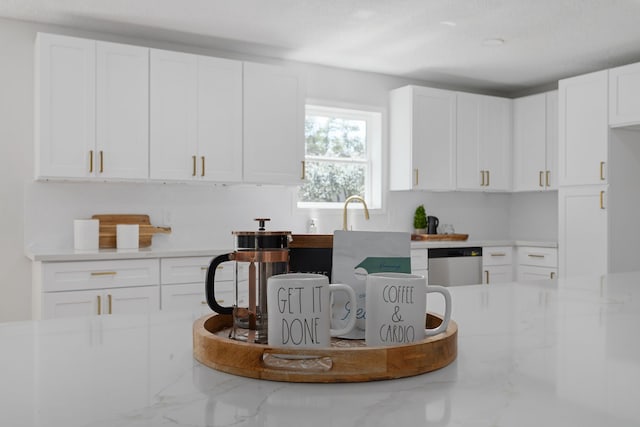 kitchen with light stone countertops, white cabinetry, and stainless steel dishwasher