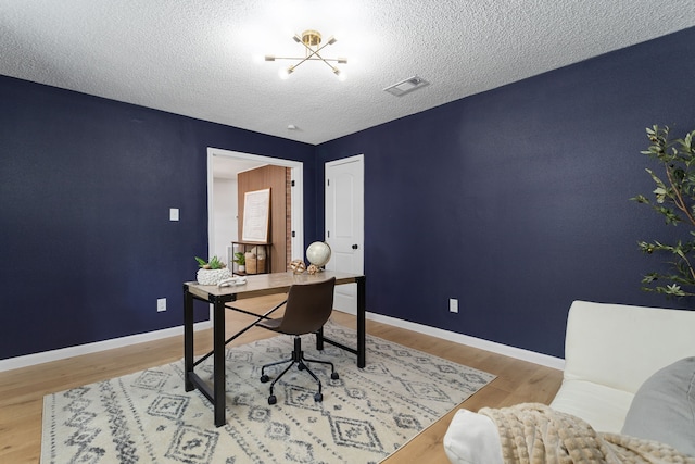 home office with an inviting chandelier, a textured ceiling, and light wood-type flooring