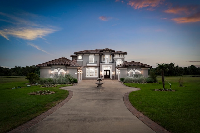 mediterranean / spanish house featuring driveway, a front yard, a tiled roof, and stucco siding