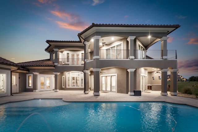 back house at dusk with a patio, french doors, and a balcony