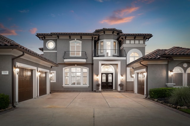 view of front of home with driveway, a garage, a tile roof, french doors, and stucco siding