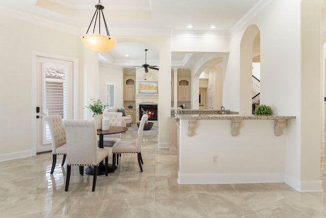 dining space featuring ornamental molding, a tray ceiling, a large fireplace, and ceiling fan