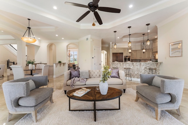 living area with arched walkways, a raised ceiling, a ceiling fan, crown molding, and recessed lighting