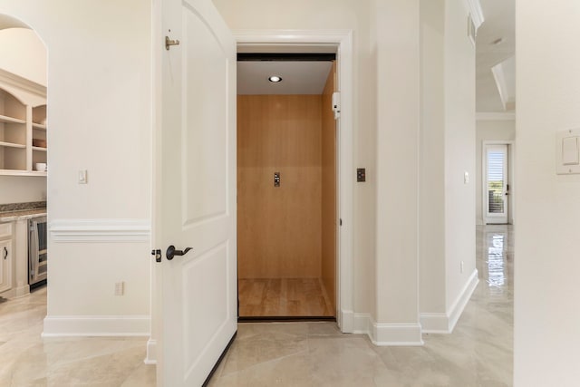 hallway with beverage cooler, baseboards, marble finish floor, ornamental molding, and elevator