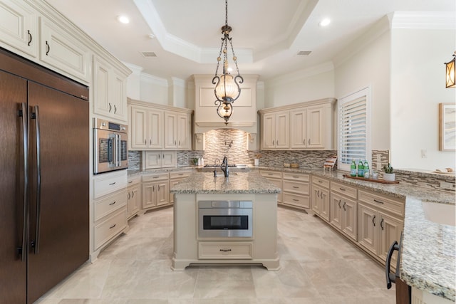 kitchen with cream cabinets, a center island with sink, built in fridge, and decorative light fixtures