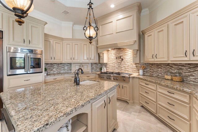 kitchen featuring light stone countertops, appliances with stainless steel finishes, cream cabinetry, and pendant lighting