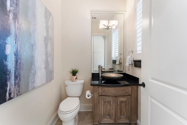 bathroom with toilet, an inviting chandelier, vanity, and tile patterned flooring