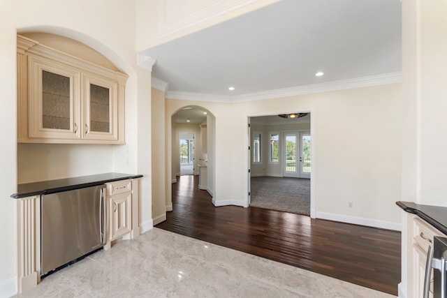 interior space with dark countertops, glass insert cabinets, refrigerator, crown molding, and cream cabinetry